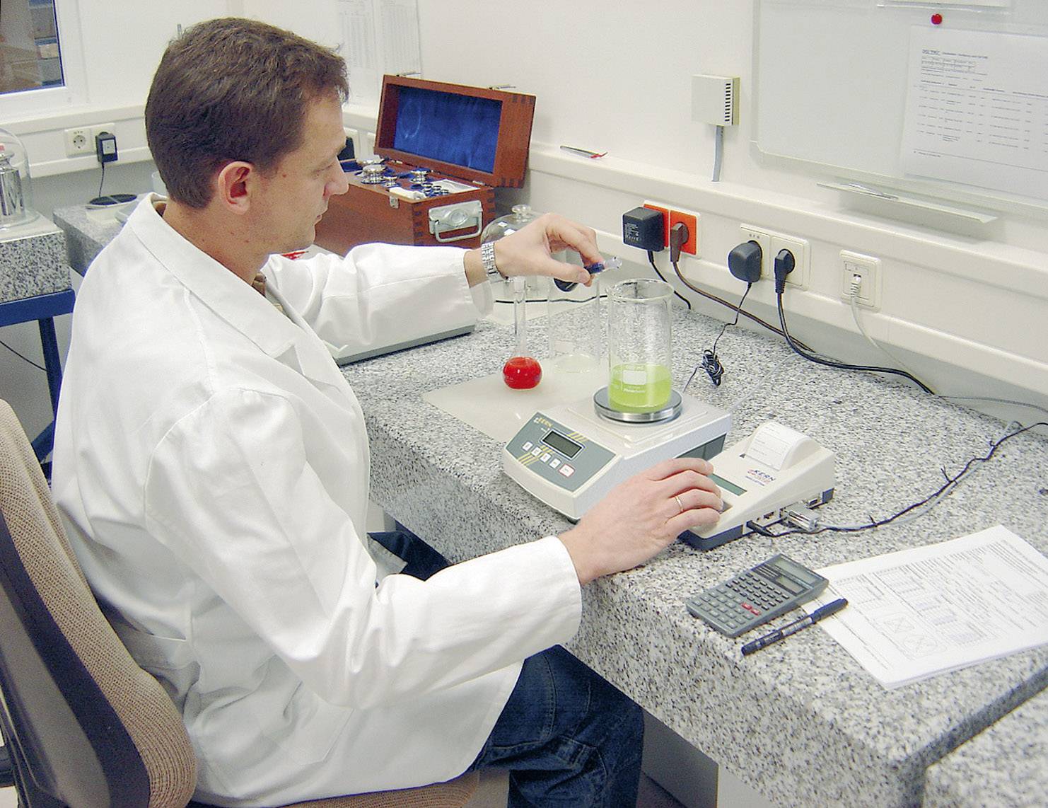 Un scientifique en blouse blanche effectue une mesure chimique avec un bécher et un appareil d'analyse dans un laboratoire.