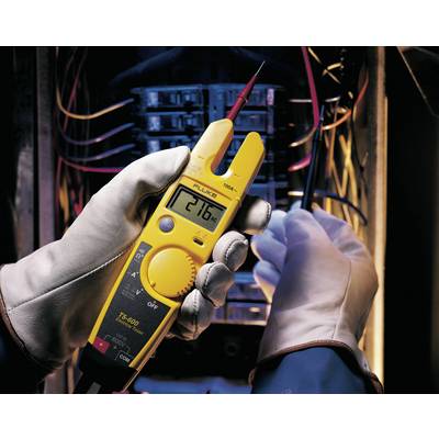 Une personne portant des gants de sécurité mesure la tension dans un boîtier électrique à l'aide d'un multimètre jaune.