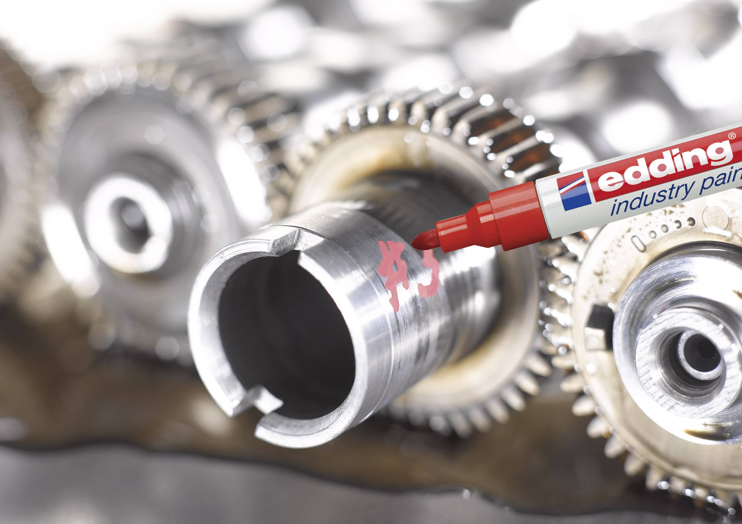 Un marqueur industriel rouge écrit sur une surface métallique à côté d'engrenages. L'accent est mis sur la précision et la durabilité dans un environnement industriel.