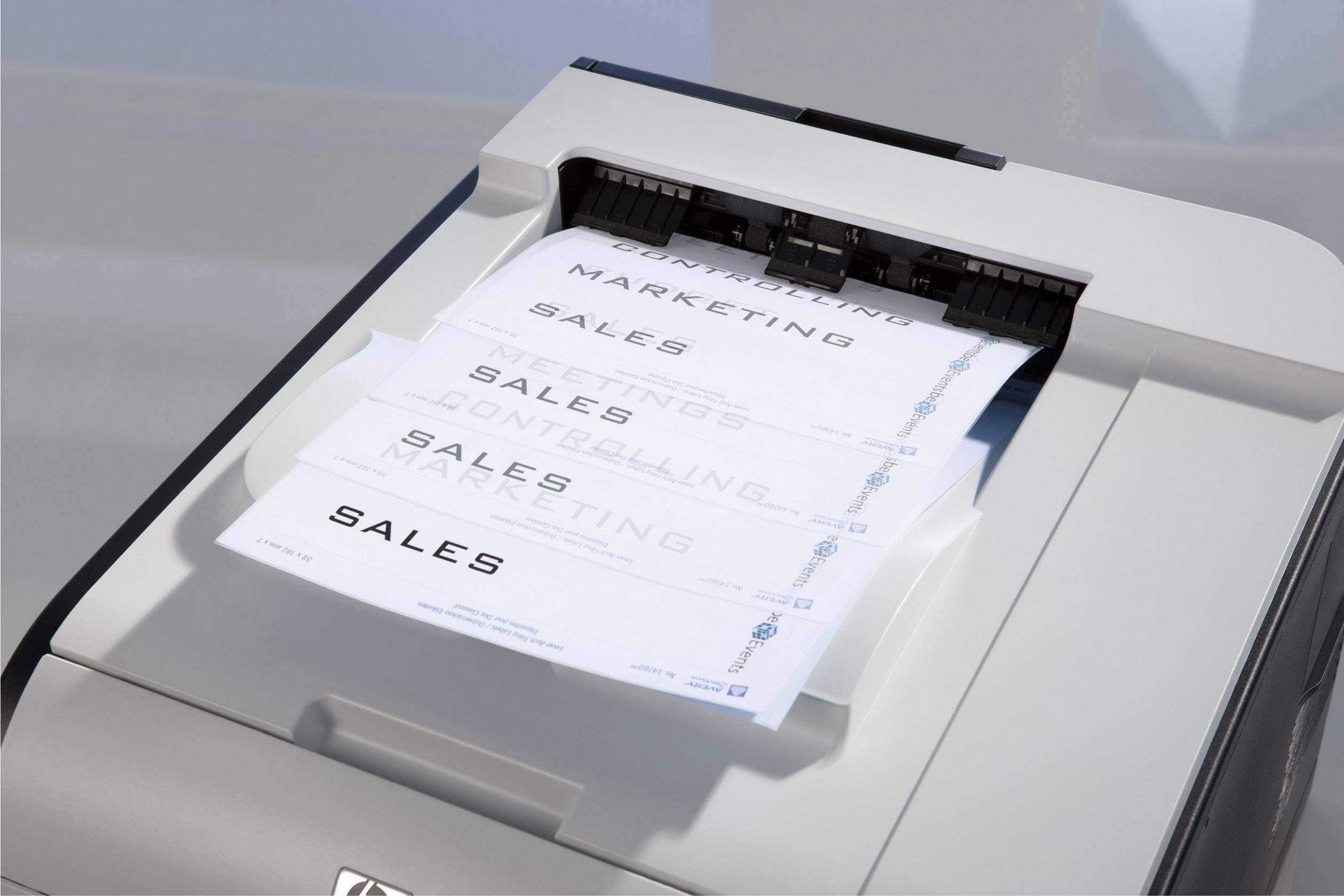 Une imprimante produit plusieurs pages portant le mot 'SALES', qui sont empilées dans un bac de sortie. L'image illustre le processus d'impression.