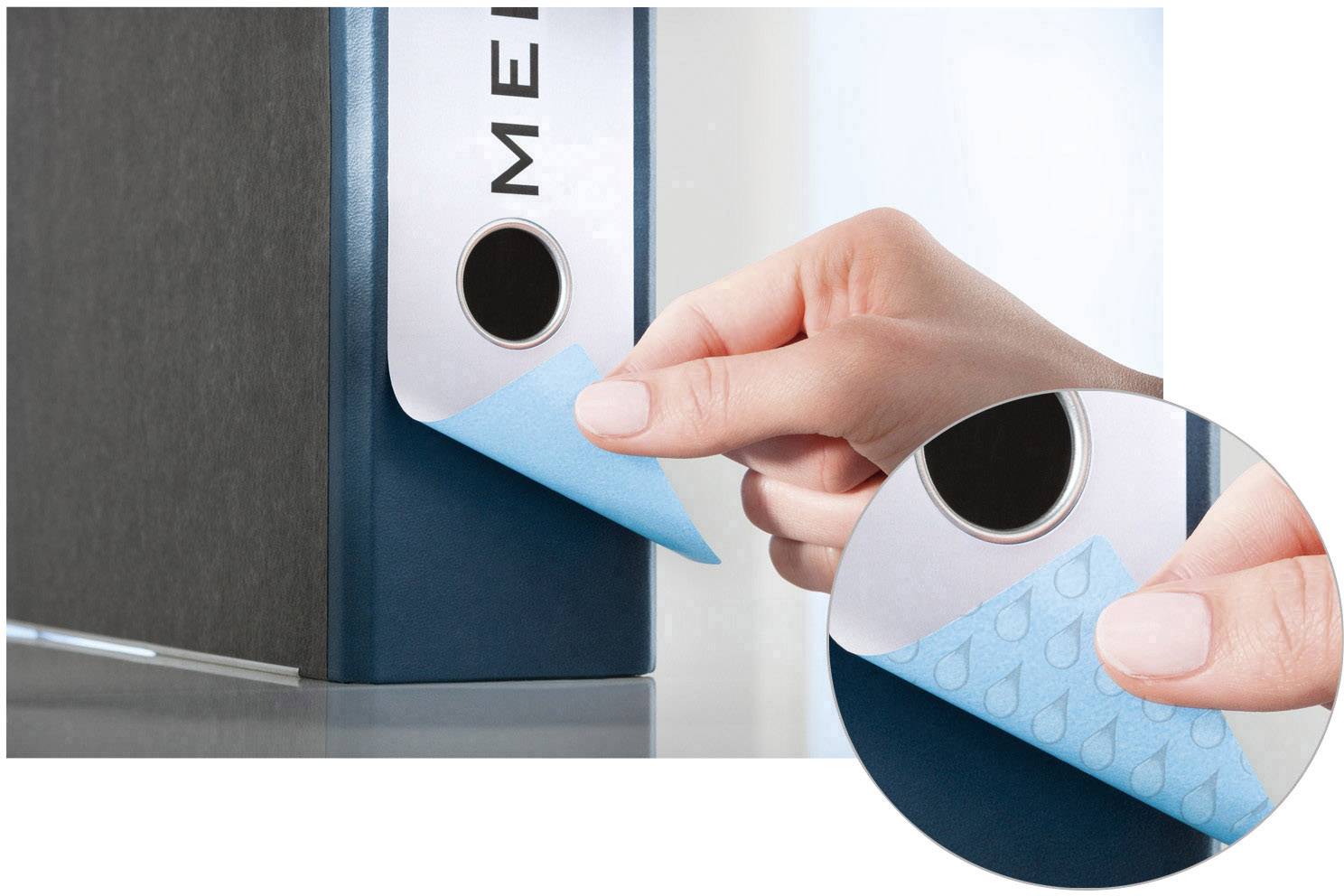 Un classeur bleu est étiqueté avec un petit post-it bleu. Une main colle la note, gros plan sur les doigts et le post-it.