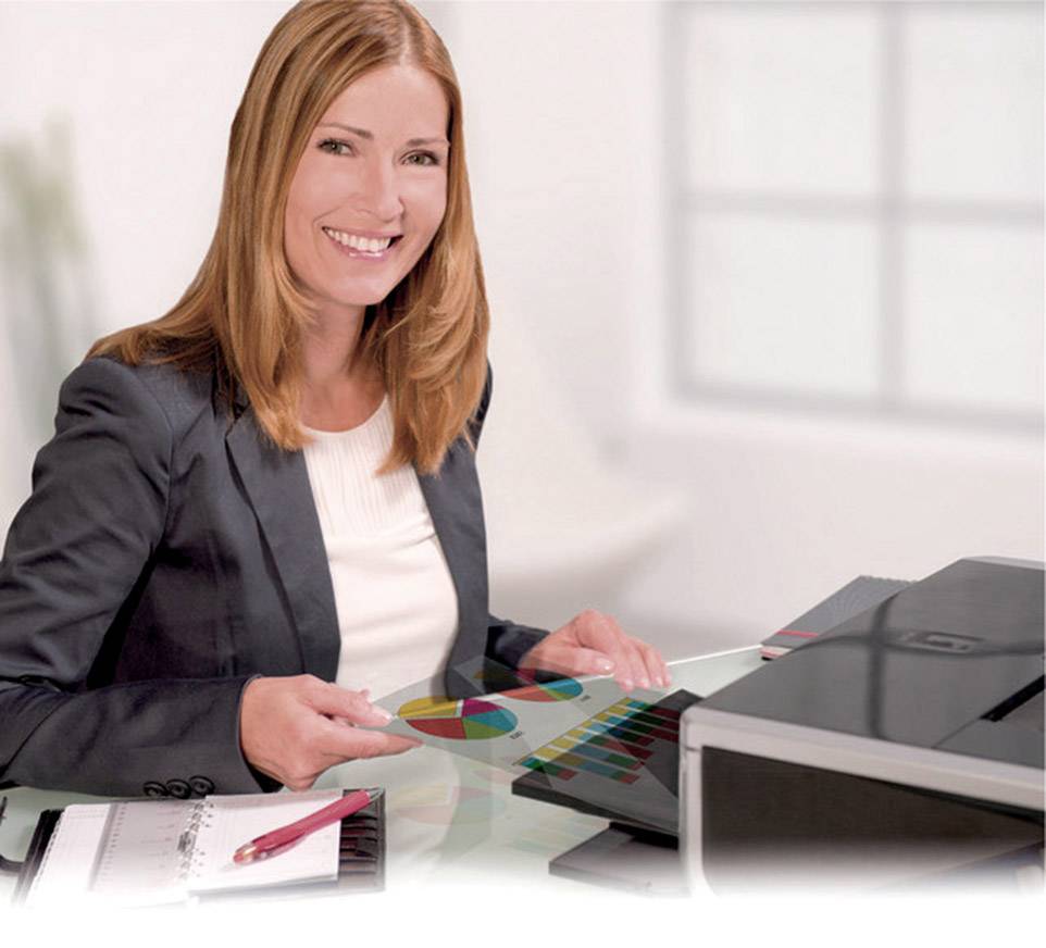 Une femme est assise à un bureau et pointe un diagramme circulaire coloré. Devant elle se trouvent un ordinateur portable, un bloc-notes et un stylo.