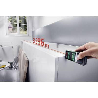 Une main tient un télémètre laser affichant la longueur d'un plan de travail de cuisine à '3,395 m'. Outils en arrière-plan.