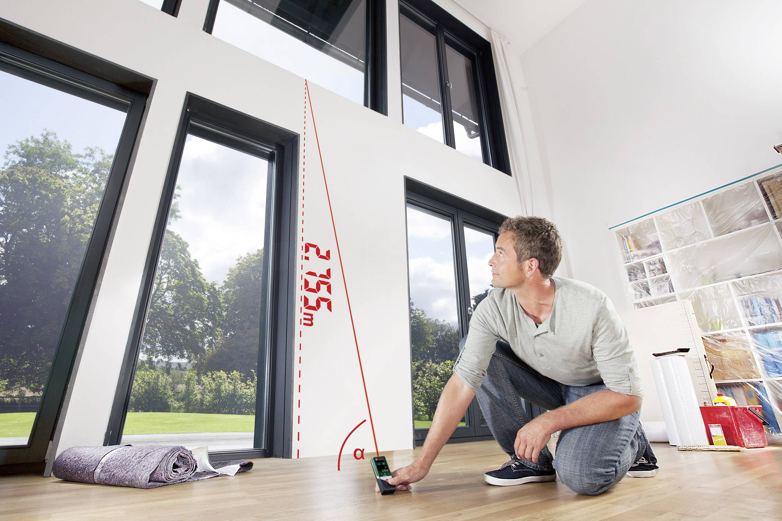 Un homme mesure la hauteur d'une grande fenêtre dans la pièce à l'aide d'un télémètre laser. La hauteur est de 2,75 m.
