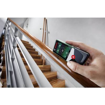 Une personne mesure la longueur d'une rampe en bois à l'aide d'un télémètre laser numérique sur un escalier.
