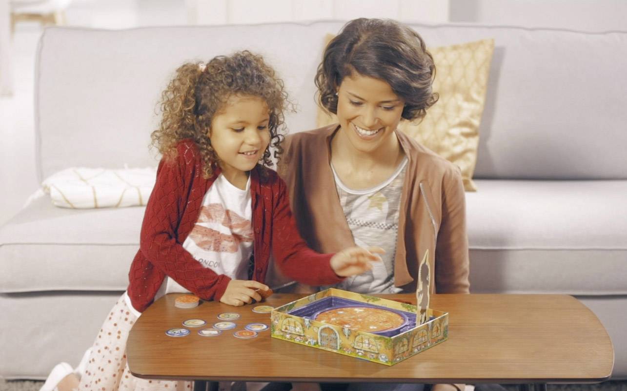 Un enfant et une femme jouent ensemble à un jeu de société à table. L'enfant est enthousiaste et pointe du doigt le plateau de jeu.
