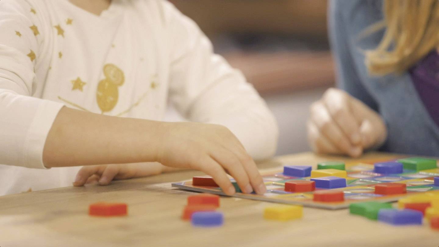 Deux enfants jouent avec des blocs de bois colorés sur une table et les disposent sur un tapis de jeu.