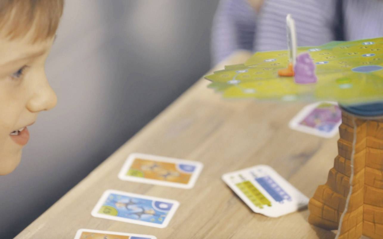 Un enfant joue à un jeu de société avec des cartes et une plateforme surélevée en forme de tour, sur laquelle sont placées de petites figurines.