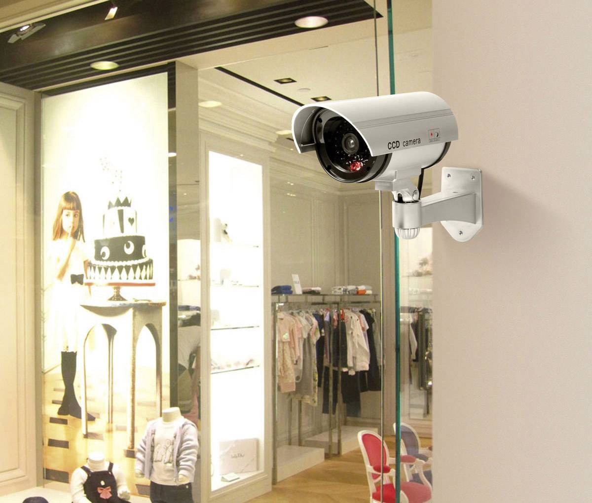 Caméra de surveillance fixée au mur surveillant l'intérieur d'une boutique de vêtements, avec des vêtements pour enfants et des articles de décoration visibles.