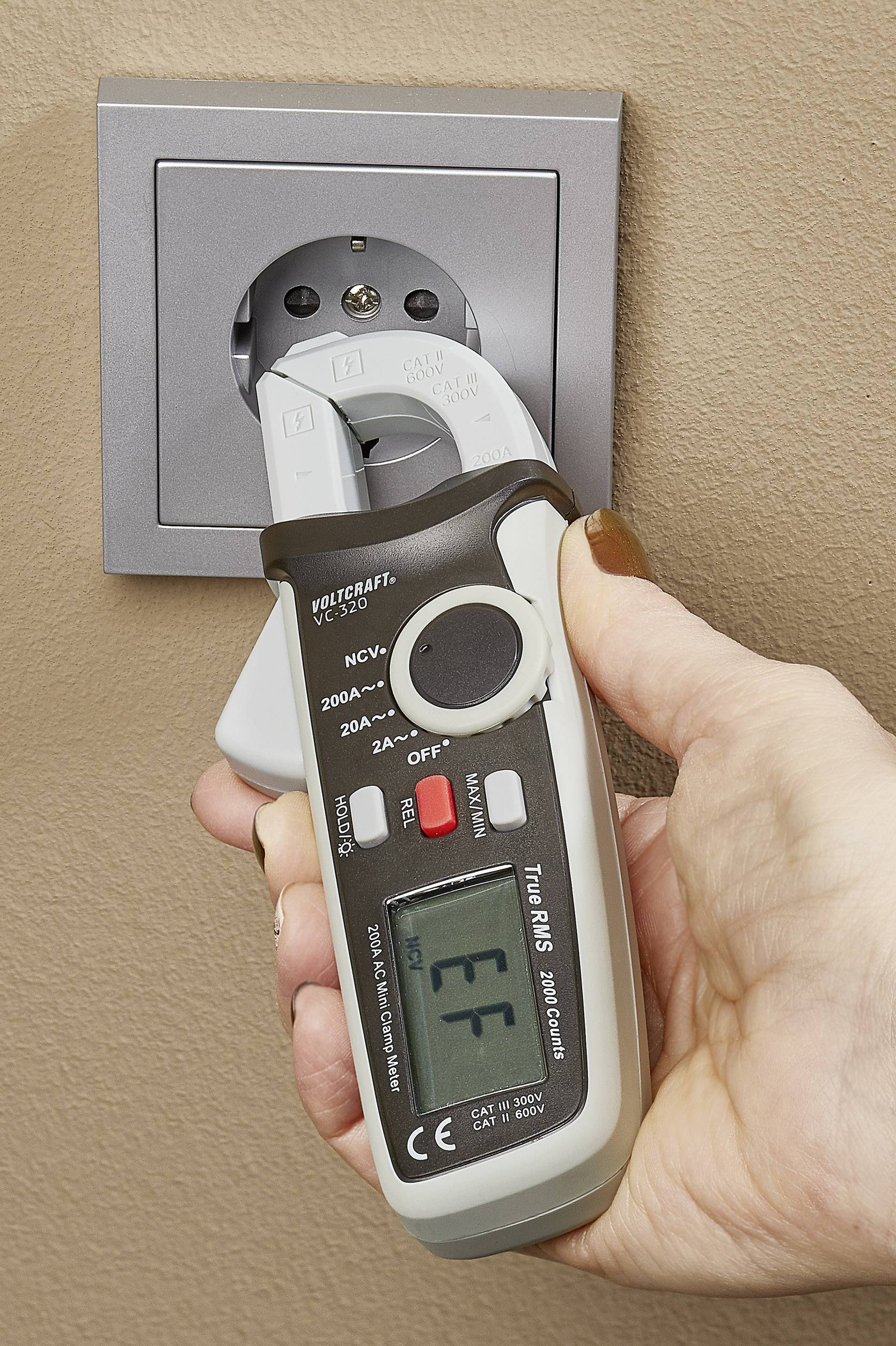 Une main tient un appareil de mesure numérique branché dans une prise de courant pour mesurer le flux électrique.