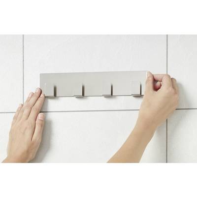 Des mains fixent une barre métallique avec des crochets sur un mur carrelé.