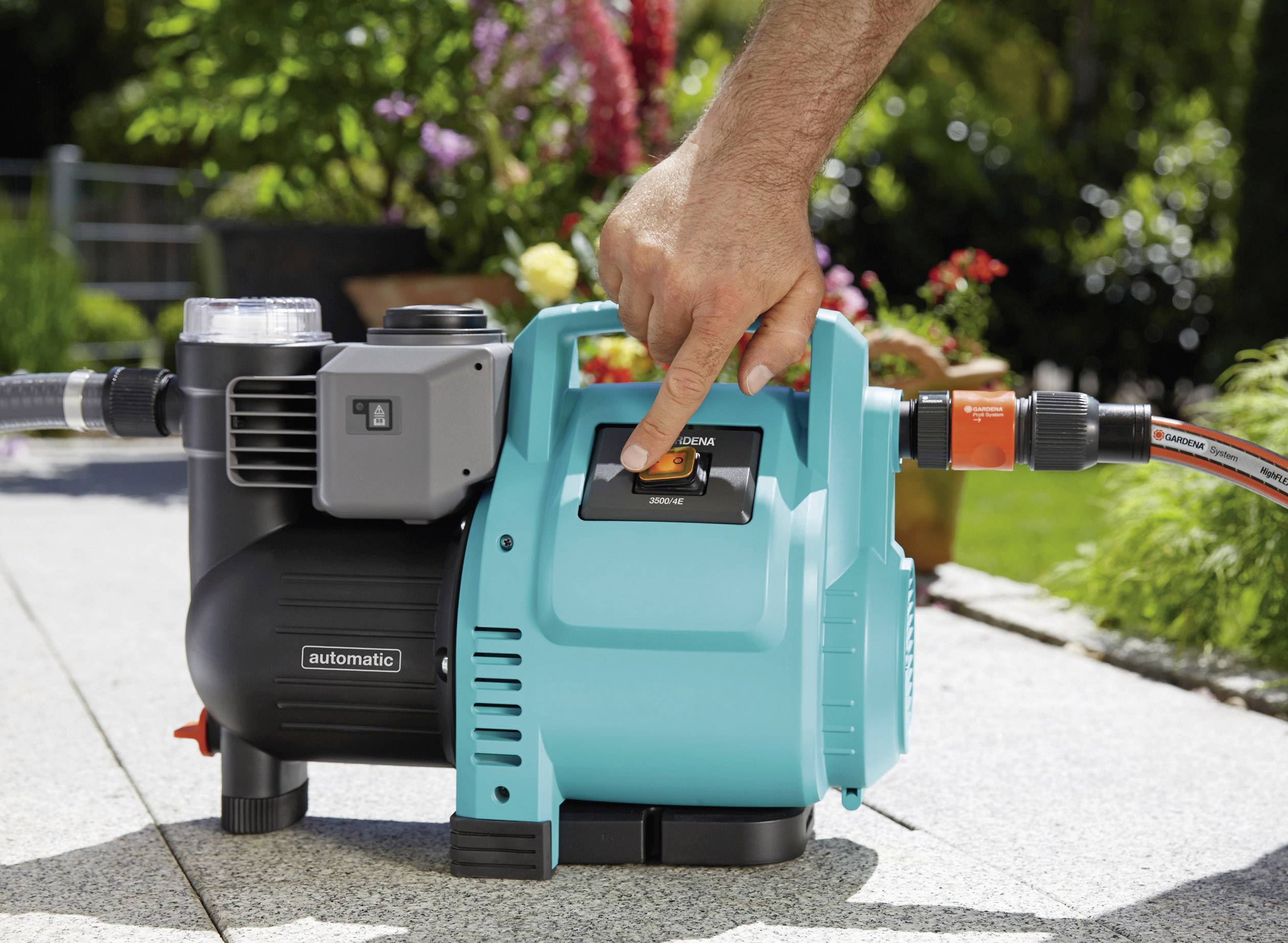 Une personne utilise une pompe à eau électrique dans le jardin. La pompe comporte des pièces bleues et noires et est raccordée à un tuyau.