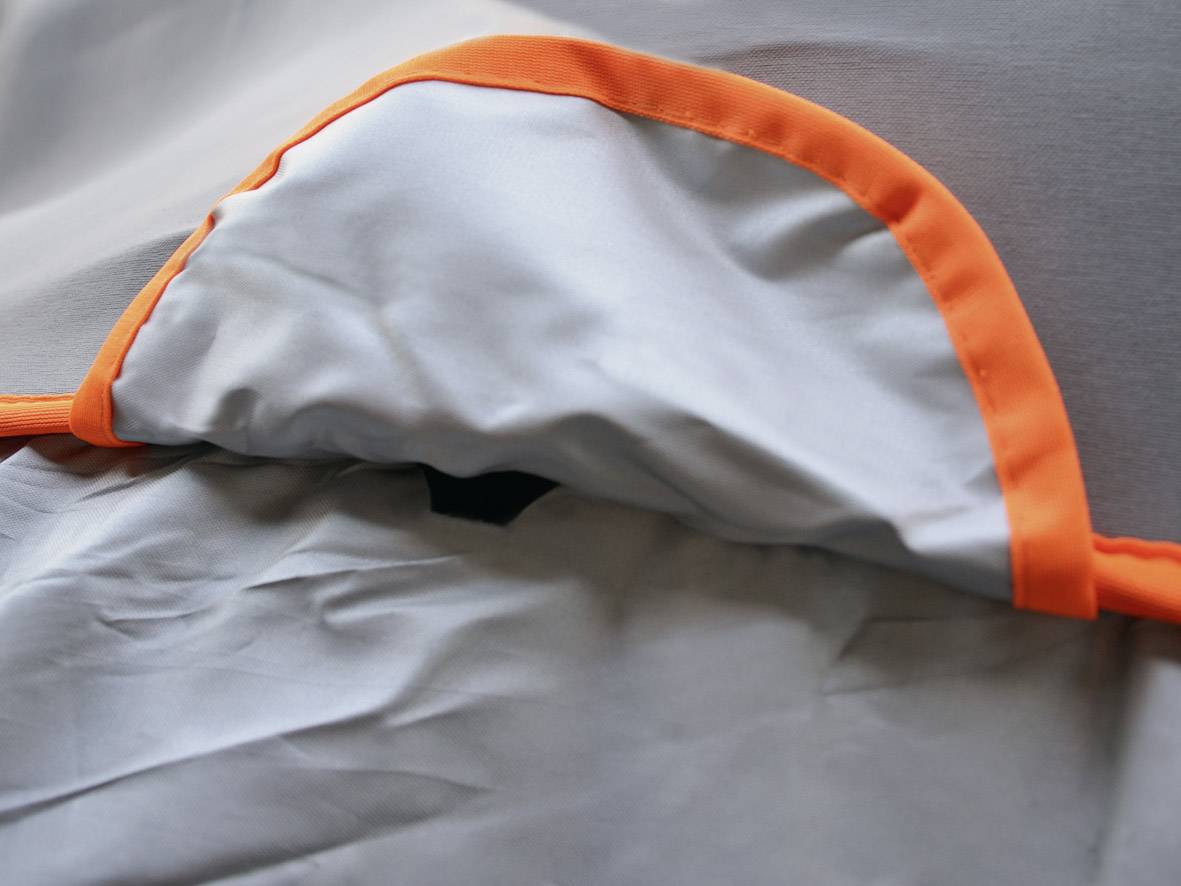 Un morceau de tissu gris avec un bord orange vif est posé à plat. Des plis légers sont visibles en arrière-plan.