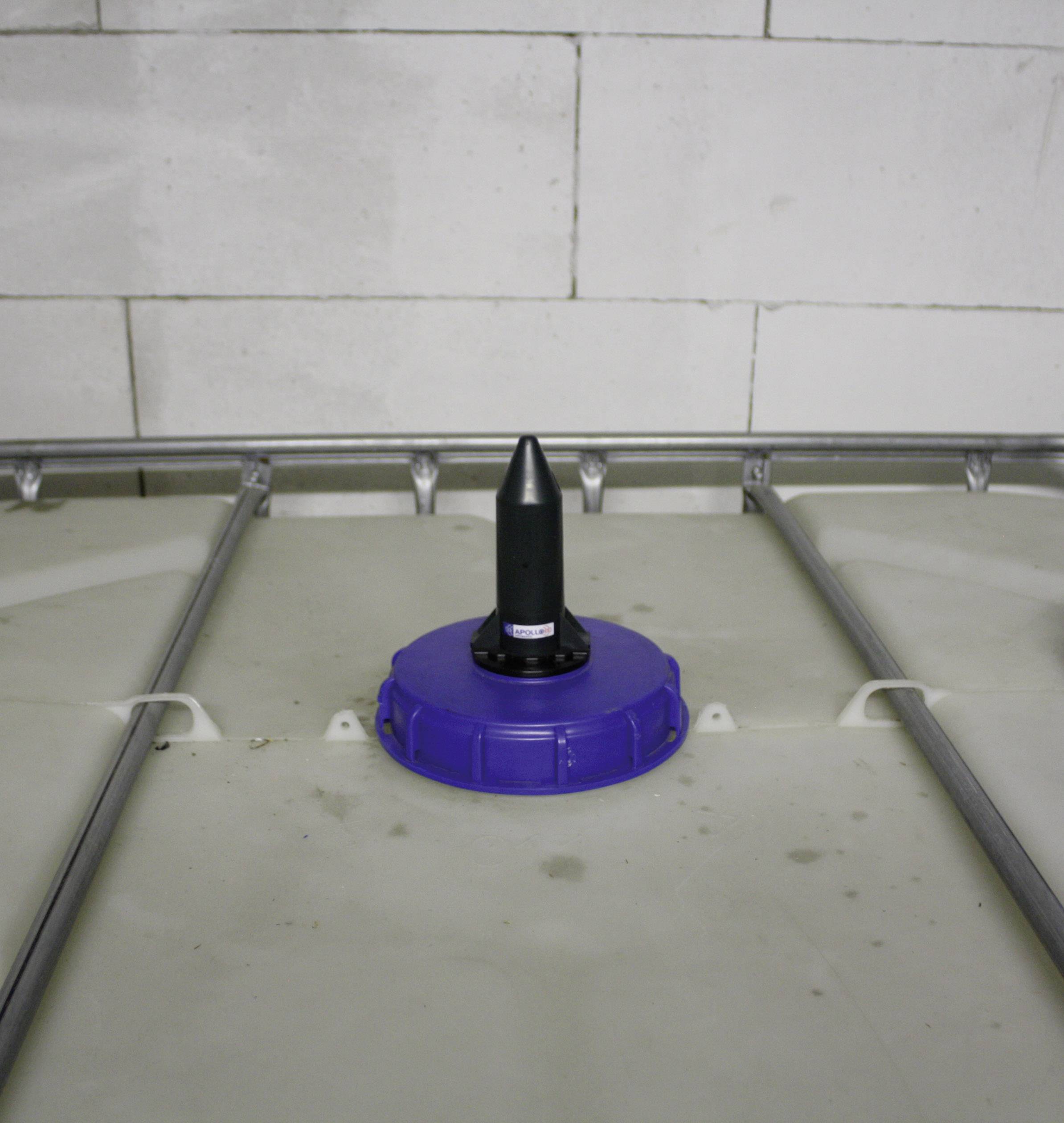 Couvercle en plastique bleu avec un accessoire noir sur un grand récipient en plastique devant un mur blanc.