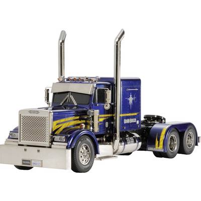 Un camion bleu avec des bandes jaunes est stationné sur une route. Le camion possède deux tuyaux d'échappement chromés et hauts.