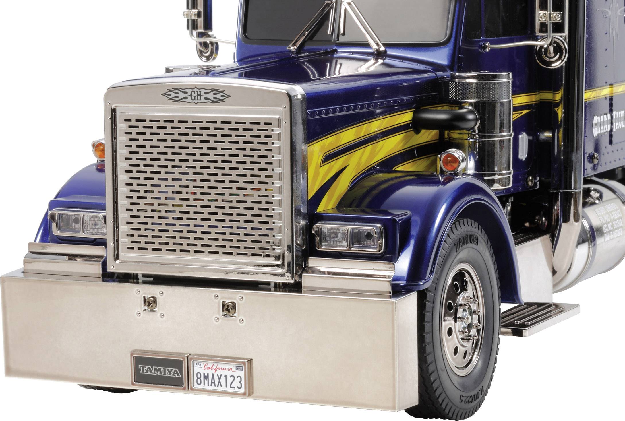 Grand camion bleu avec des bandes jaunes sur le capot et un grand couvercle de radiateur argenté. Des panneaux de détails et des phares sont visibles.