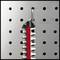 Un peigne rouge et noir est suspendu à un crochet sur un mur métallique perforé.