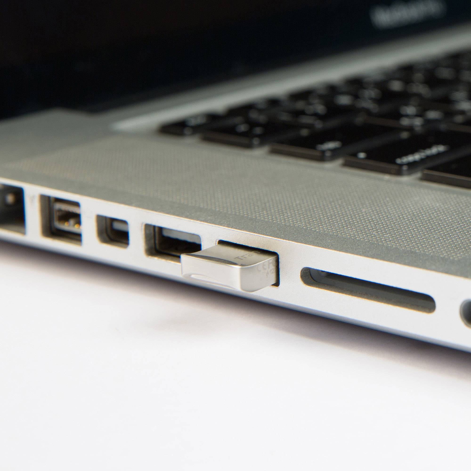 Une clé USB est branchée dans le port USB d'un ordinateur portable. L'ordinateur portable est de couleur argent et une partie du clavier est visible.