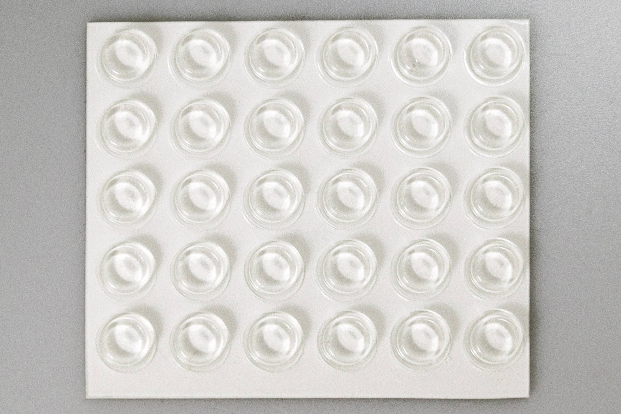 Une rangée de butoirs en plastique transparent sur un support blanc. Ils sont disposés symétriquement et servent de protection ou d'entretoises.