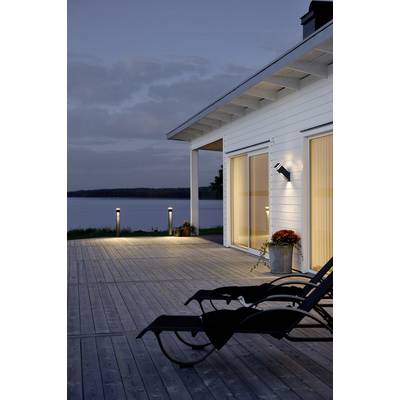 Maison moderne avec terrasse en bois au crépuscule, deux chaises longues au premier plan, vue sur le lac en arrière-plan, éclairage allumé.