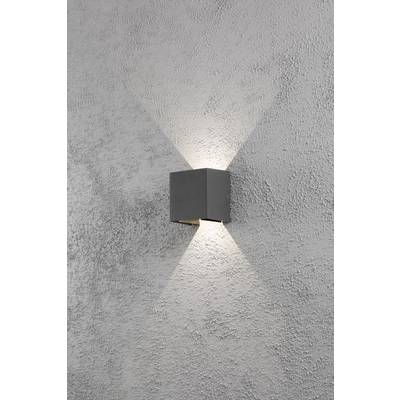 Une lampe murale grise projette un motif lumineux en forme de X sur un mur gris à la texture rugueuse.