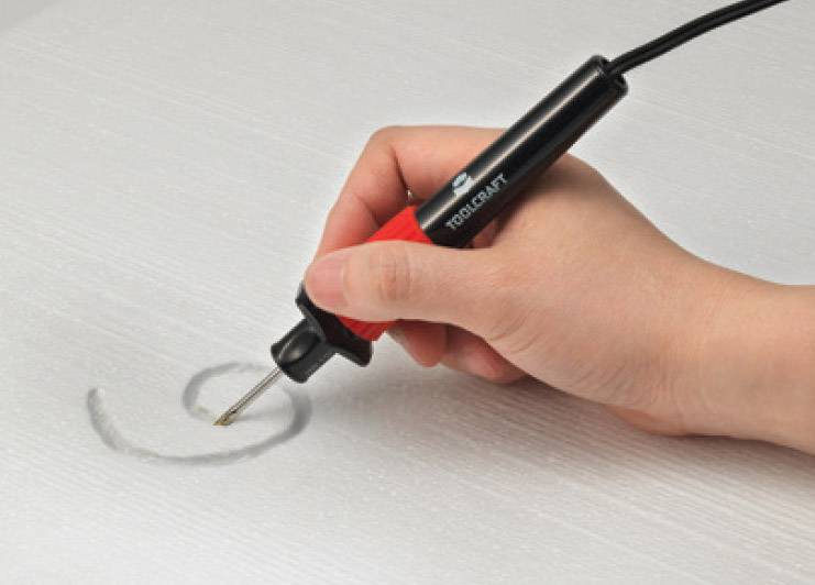 Une main tient une machine à graver rouge et noire et grave un cercle sur une surface lisse et grise.