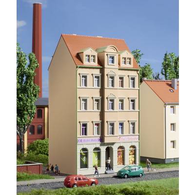 Immeuble résidentiel sur plusieurs étages avec des commerces au rez-de-chaussée ; une cheminée à gauche et des arbres en arrière-plan ; deux voitures sont garées devant.