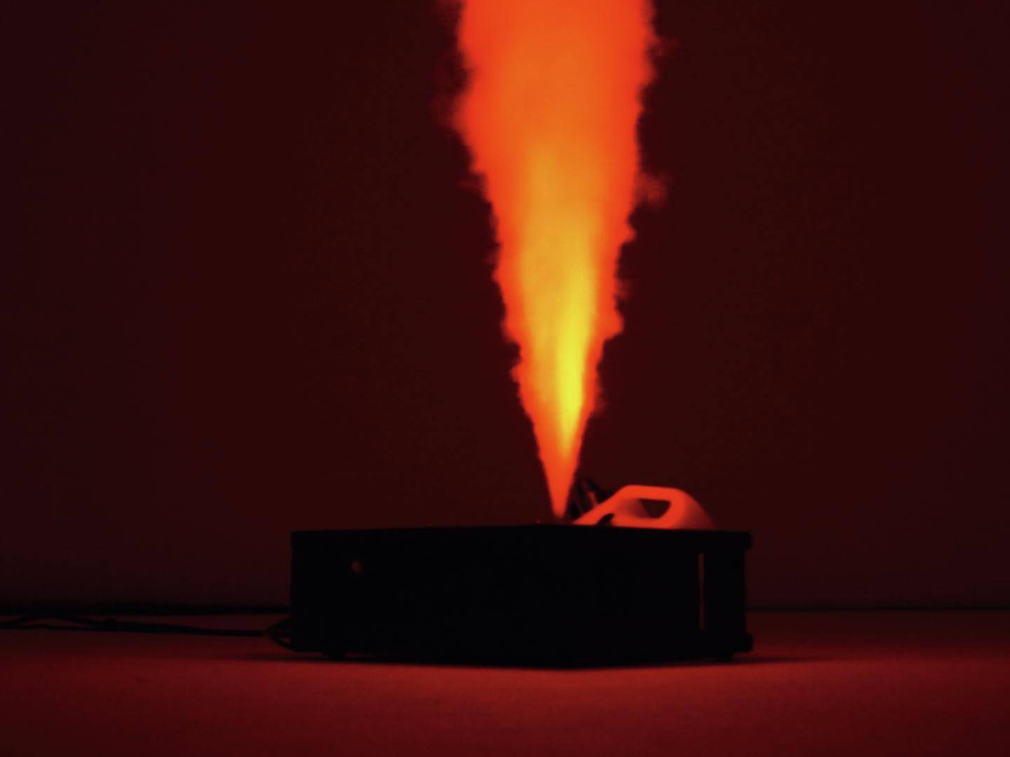 Un appareil émet un nuage de fumée verticalement, lumineux et orange, dans une pièce sombre.