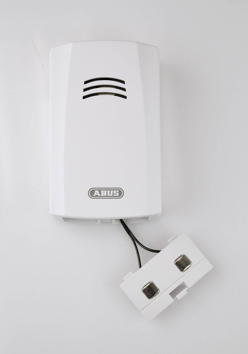 Détecteur de fumée clair avec grille de ventilation noire et câble pendant, monté sur un mur blanc.