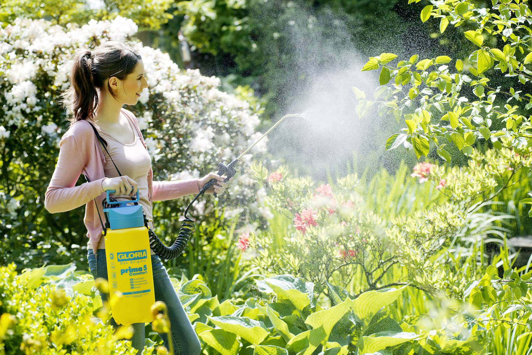 Une femme vaporise des plantes dans un jardin à l'aide d'un pulvérisateur. Elle porte des vêtements décontractés et est concentrée sur son travail.