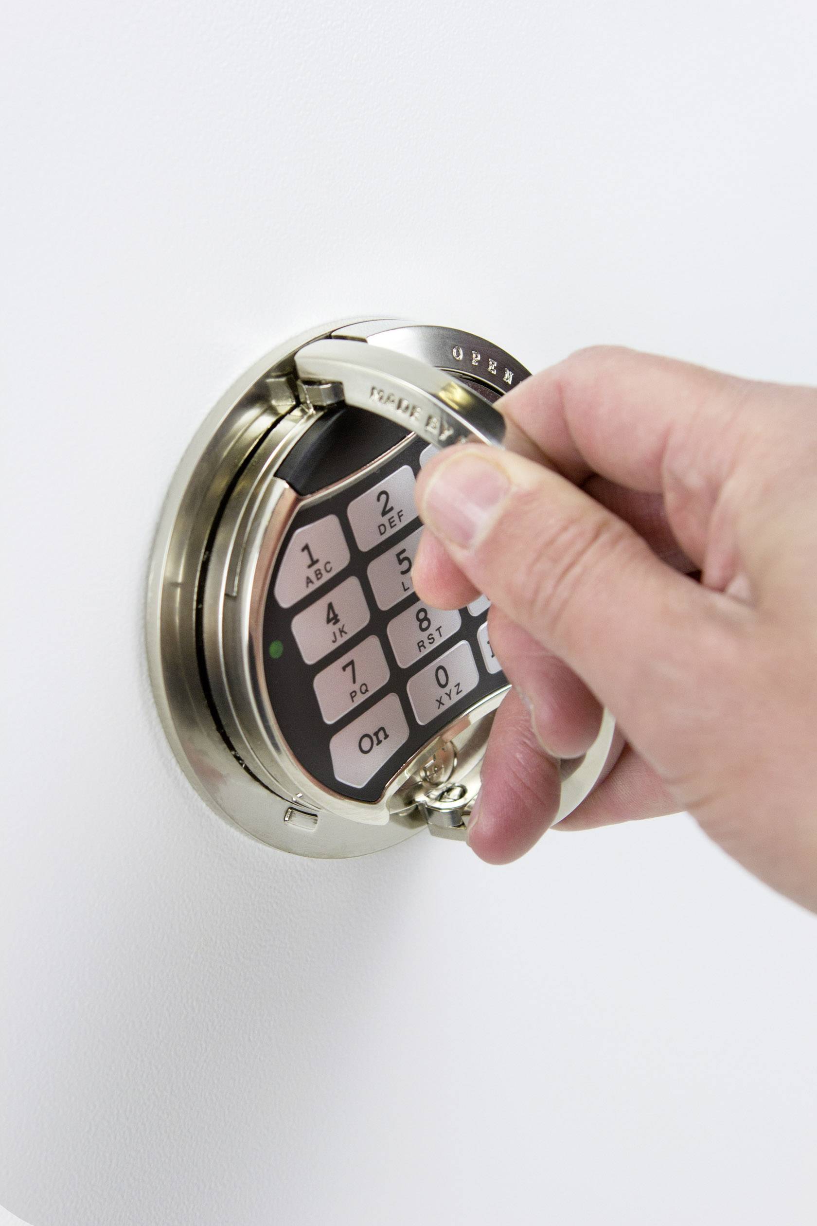Une main fait tourner un disque sur un verrou électronique de coffre-fort avec clavier numérique pour ouvrir ou sécuriser le coffre.