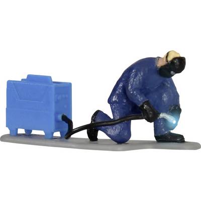 Miniature d'un soudeur agenouillé en bleu de travail, travaillant avec un appareil de soudage. L'homme porte un masque de protection.