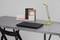 Un bureau gris avec un ordinateur portable noir, une lampe de bureau et un range-documents contenant des classeurs et des cahiers.