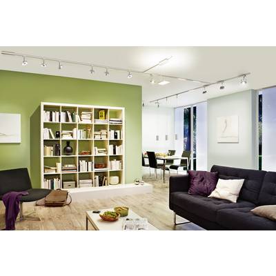 Un salon moderne avec un mur vert et une étagère remplie de livres, un canapé élégant, des luminaires au plafond et un coin repas à l'arrière-plan.