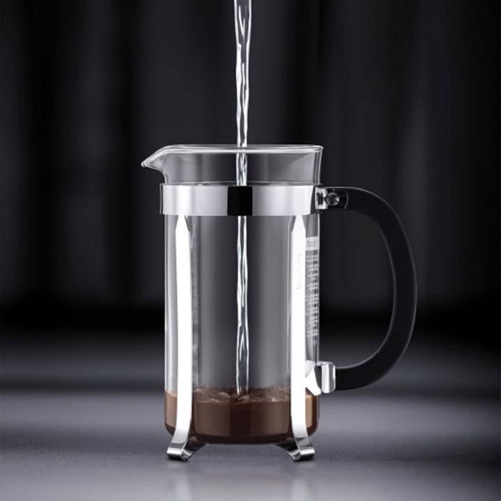 L'eau est versée dans une cafetière à piston vide contenant du café moulu au fond.