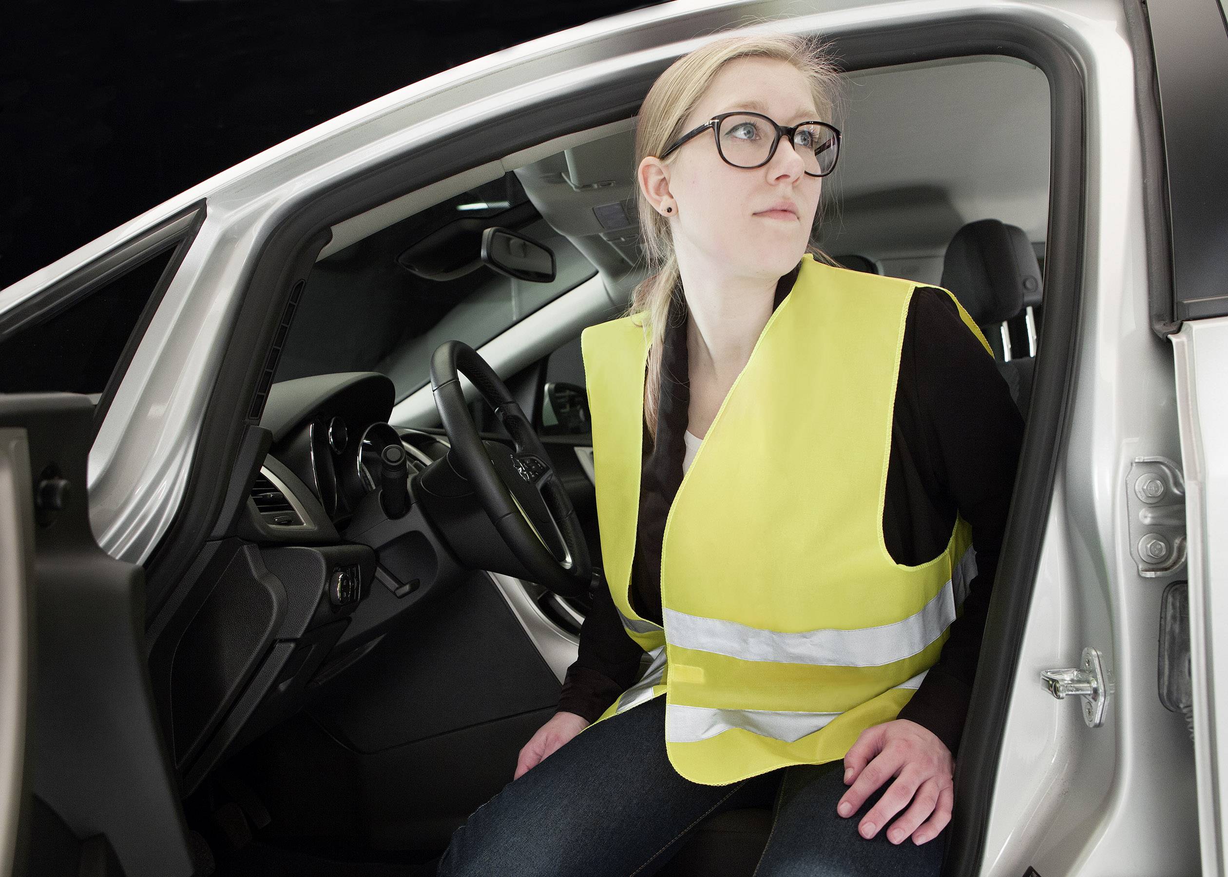 Une personne portant un gilet jaune de sécurité est assise dans une voiture et regarde à l'extérieur, comme si elle se préparait à descendre.