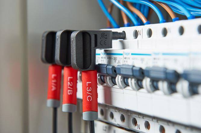 Boîte de distribution électrique avec plusieurs fusibles et câbles connectés. Des étiquettes rouges indiquent différents circuits électriques.