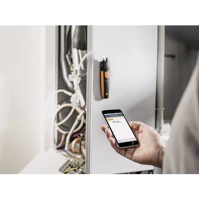 Une personne mesure les valeurs d'une chaudière à l'aide d'un smartphone et d'un capteur connecté. Les chiffres sont visibles à l'écran.