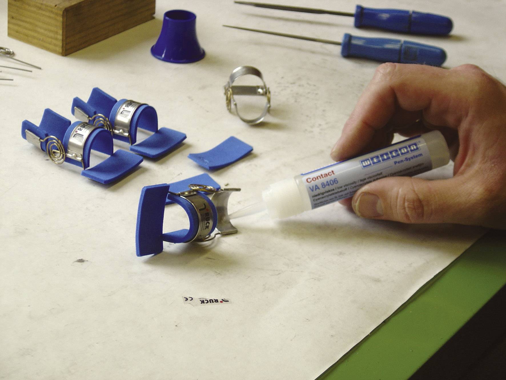 Une main applique de la colle sur une pièce métallique. Sur la table se trouvent des bracelets de montre bleus et des outils. Scénario d'un atelier de réparation.
