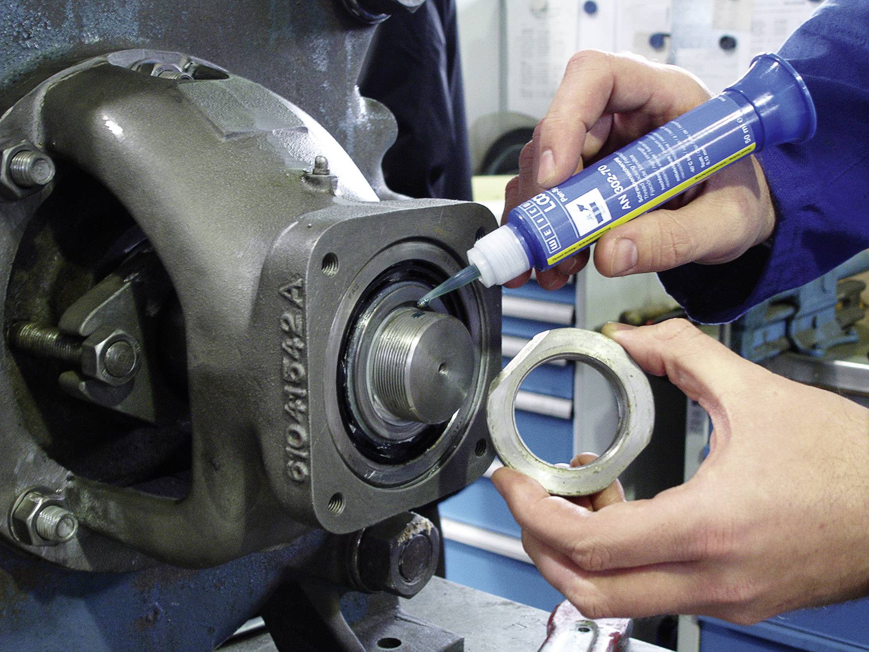 Un mécanicien applique un produit d'étanchéité sur un boîtier de machine tout en tenant un joint. Technique et précision dans la maintenance.