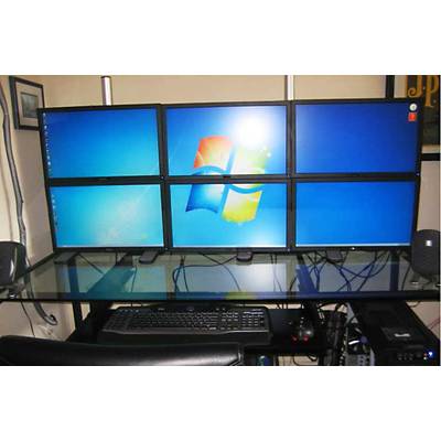 Un poste de travail avec six écrans affiche le logo Windows sur un fond bleu. Un clavier et une souris sont posés sur le bureau.