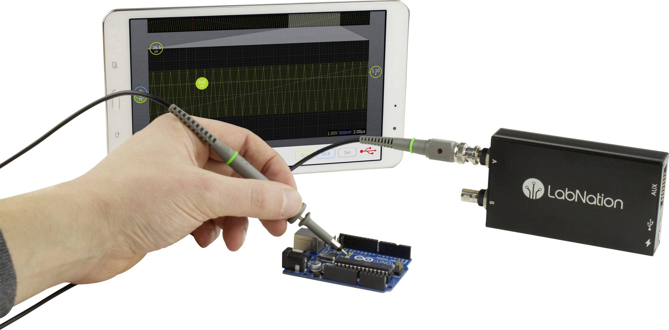 Une main manipule un oscilloscope, connecté à une carte microcontrôleur. Sur la tablette, le diagramme de mesure est visible.