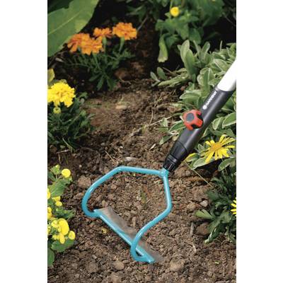 Un outil à main est utilisé dans le jardin pour ameublir le sol entre les plants de fleurs. L'outil a une tête en métal bleu.