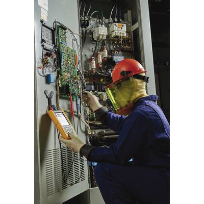 Un électricien en tenue de protection travaille avec un multimètre sur un armoire électrique ouverte remplie de câbles et de fusibles.