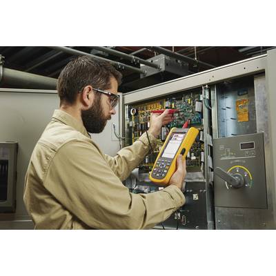 Un technicien portant des lunettes de protection utilise un multimètre pour la maintenance d'un tableau électrique dans un environnement industriel.