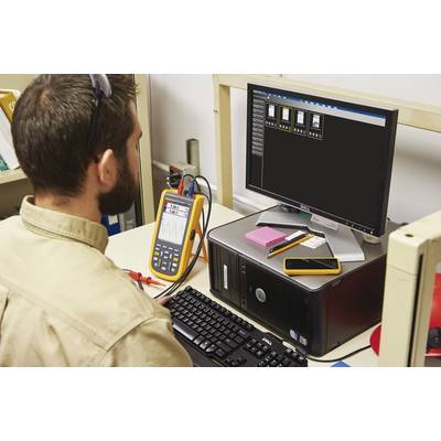 Un homme travaille sur un ordinateur avec un appareil de mesure connecté, qui affiche des données de mesure sur un écran.