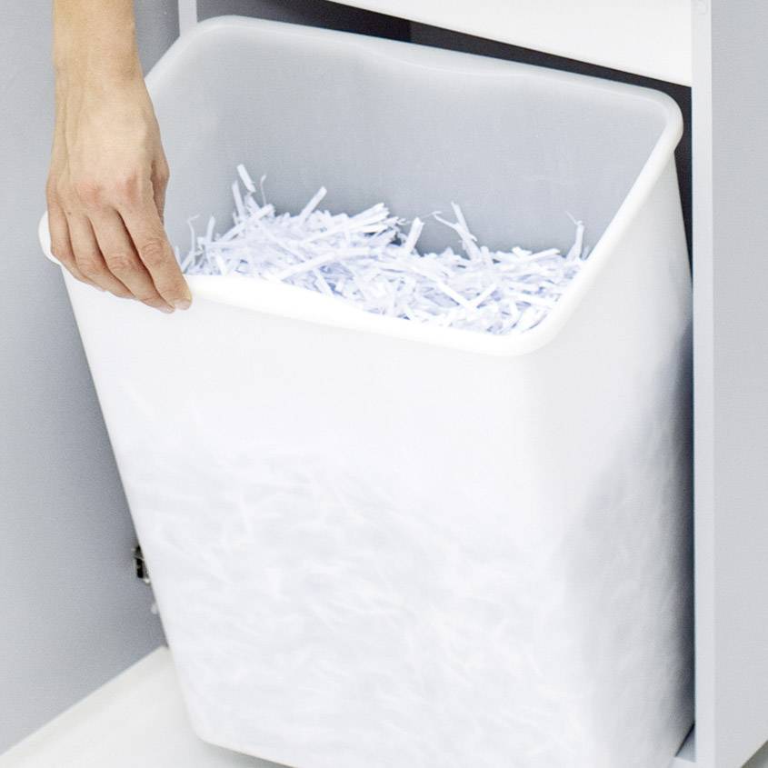 Une main retire une poubelle remplie de fragments de papier déchiquetés d'un placard.