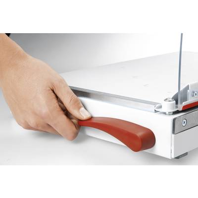 Une main actionne le levier rouge d'un massicot posé sur une table blanche.