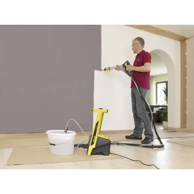 Un homme peint un mur dans une pièce à l'aide d'un pulvérisateur de peinture. Devant lui se trouve un seau de peinture. Le pulvérisateur est jaune.
