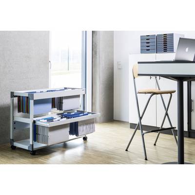 Un chariot blanc avec des touches bleues est placé près d'une fenêtre. Il est chargé de documents et de dossiers. Un table et une chaise sont visibles en arrière-plan.